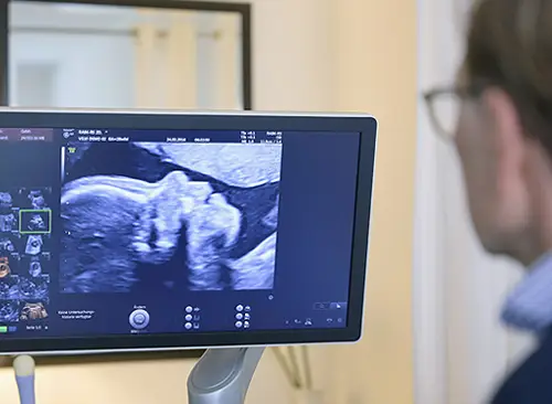 Nahaufnahme. Dr. Christian Frank sitzt vor einem Ultraschallgerät und betrachtet die Aufnahme eines ungeborenen Kindes