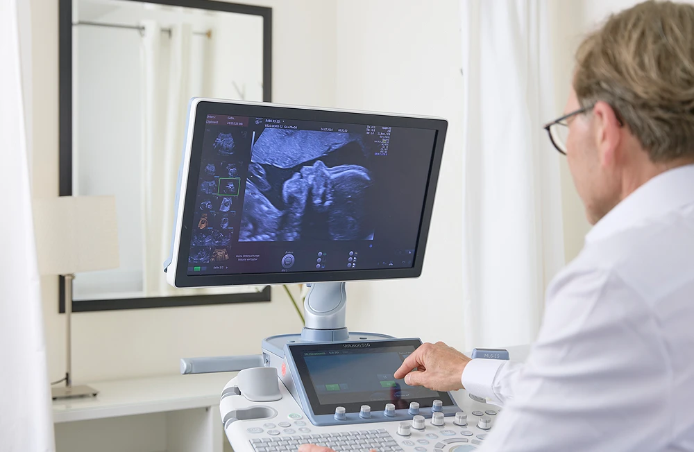 Dr. Christian Frank sitzt vor einem Ultraschallgerät und betrachtet die Aufnahme eines ungeborenen Kindes